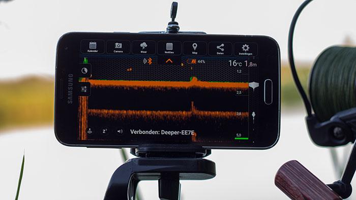 De Smartphone bevestigd op een klem van ene selfie stick (de meeste selfie sticks hebben namelijk schroefdraad voor een statief ;-)